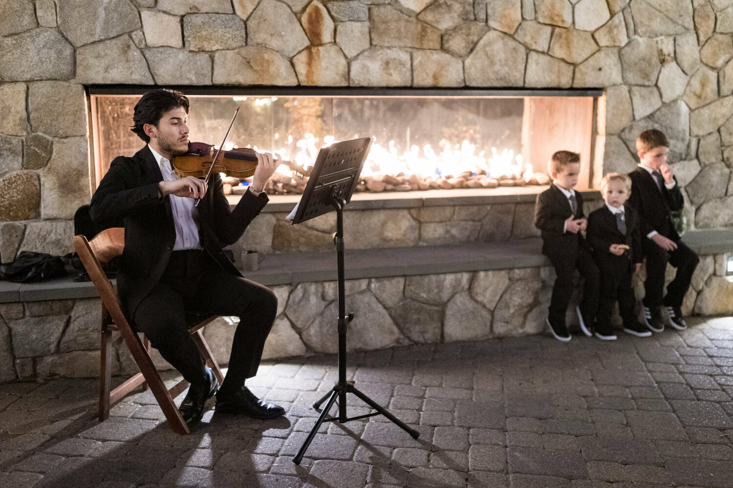 A violinist performs in front of an outdoor fireplace.
