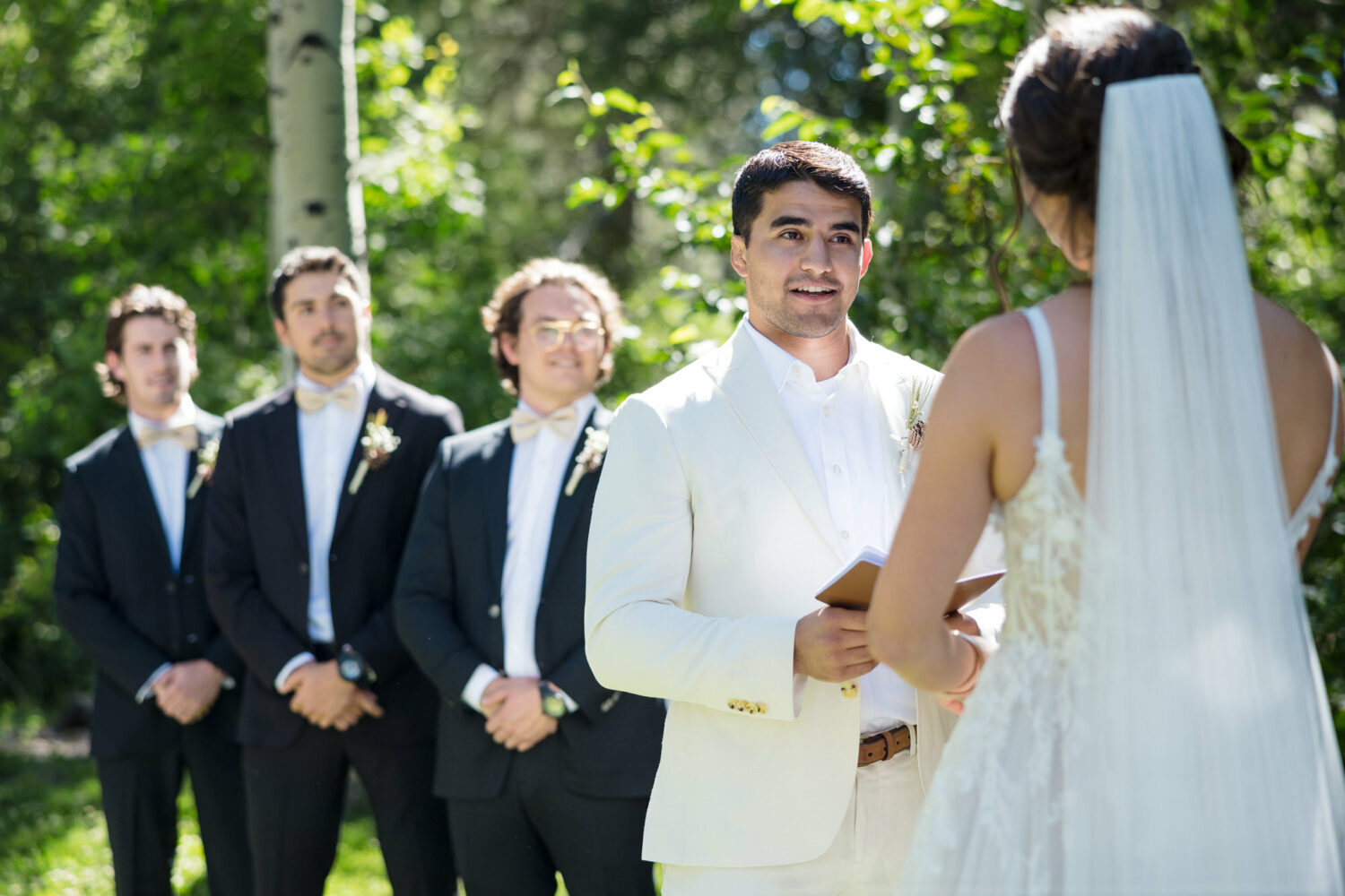 A groom reads aloud from a small notebook for personalized wedding vows.