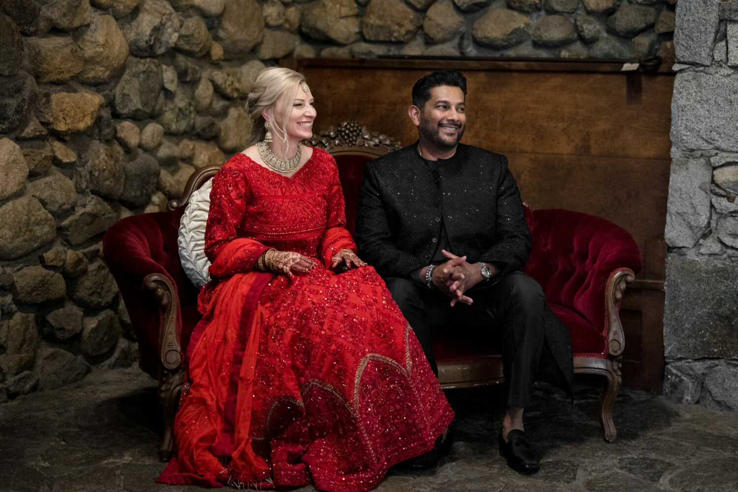 The bride and groom sit on a red velvet sofa during their Muslim wedding in Lake Tahoe.