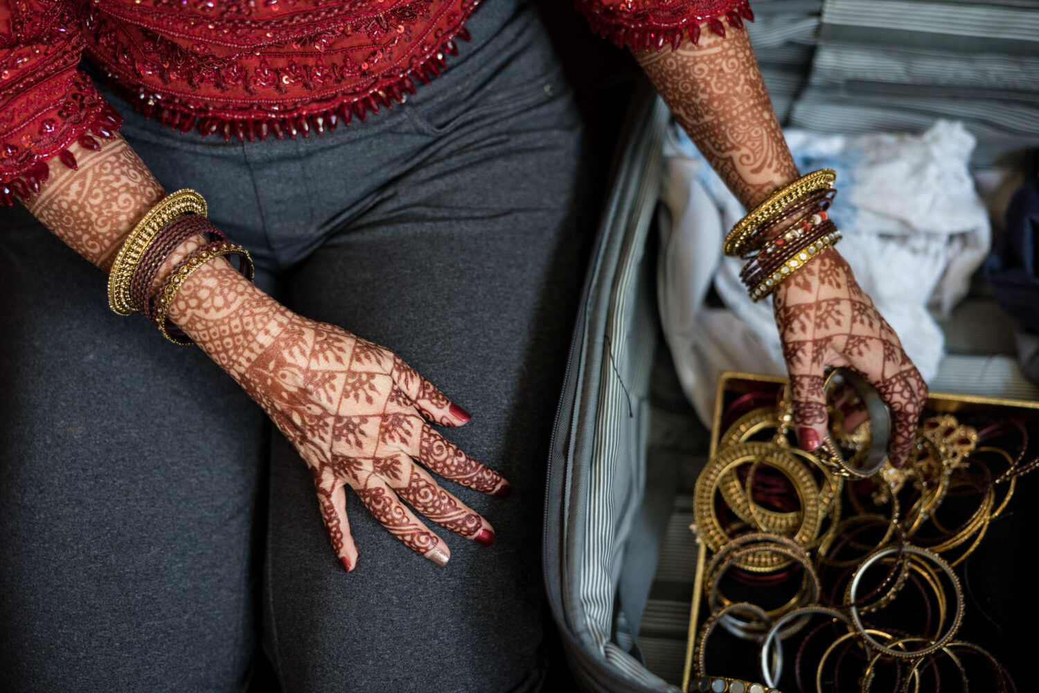 A bride's decorated henna hands choose from a box of golden wedding bangles.