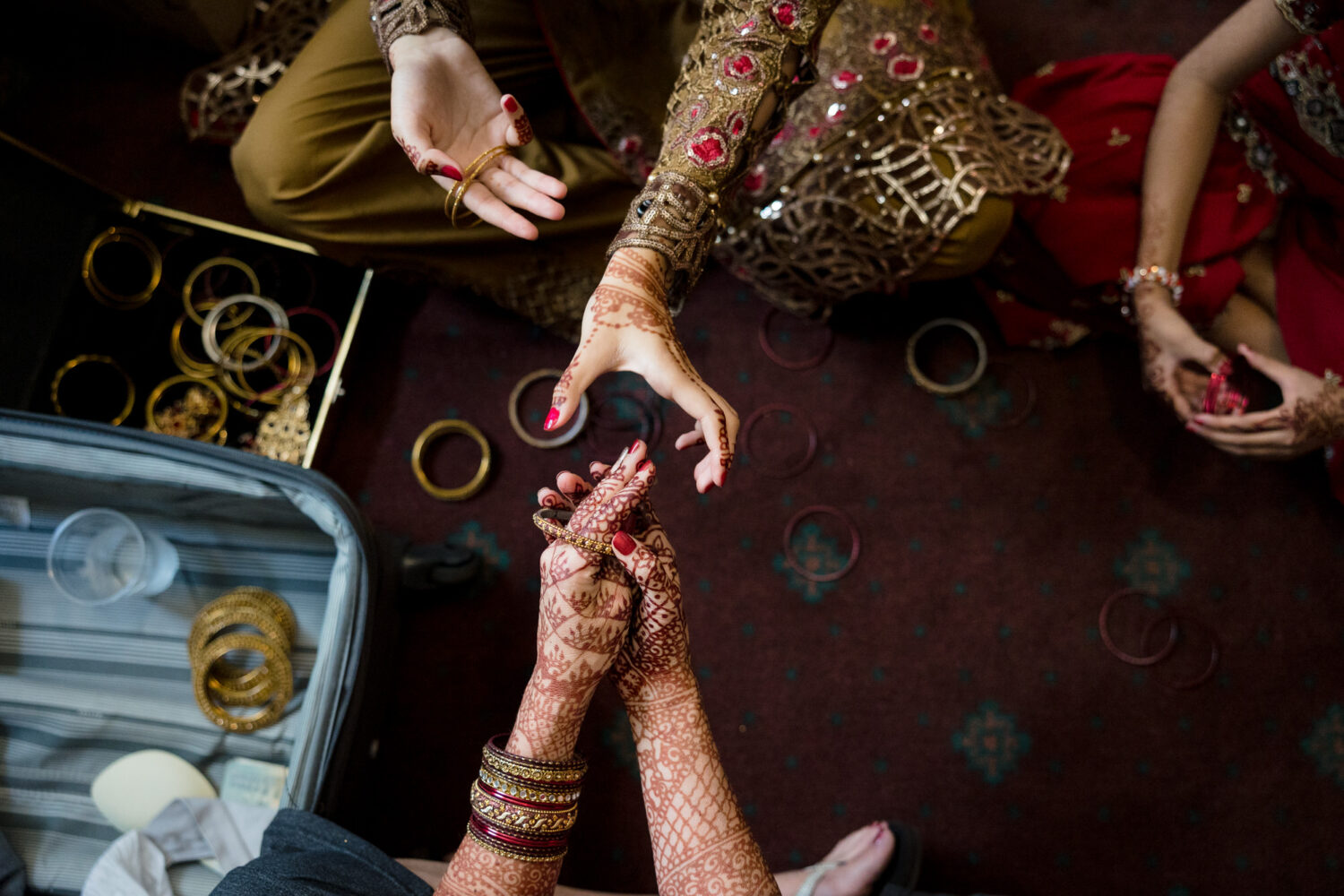 An overhead view of a bride's hands with mehndi trying on different wedding bangles. 