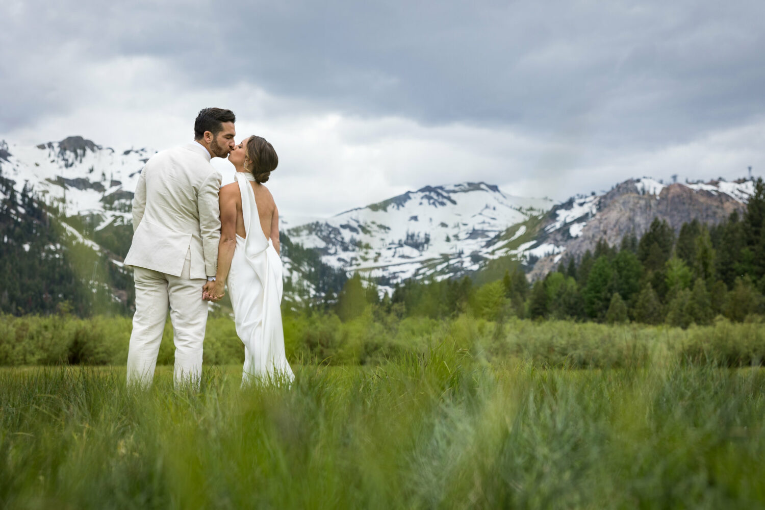 A bride and groom kiss at their first look in Olympic Valley meadows.