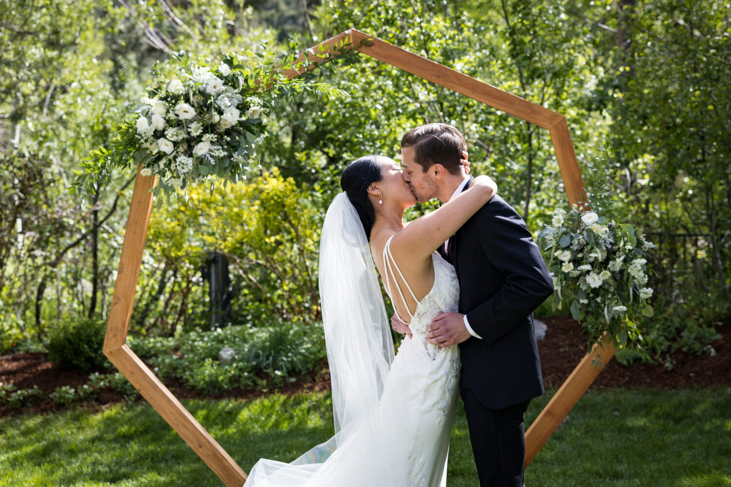 First kiss in front of a hexagon shaped arch at an Olympic Village Events Center wedding.