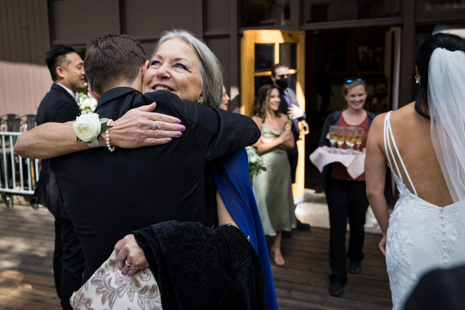 Congratulatory hugs from the mother of the groom wearing a corsage with a single white rose.