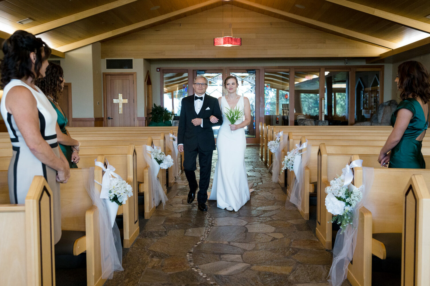 The bride and her father walk past DIY church pew decorations with white flowers.