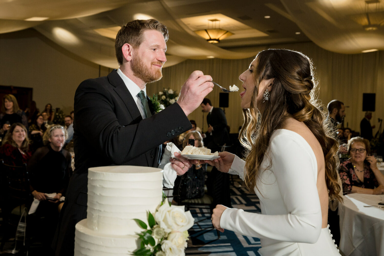 The groom feeds the bride a slice of wedding cake at their reception in the Grand Sierra Ballroom at Everline Resort.