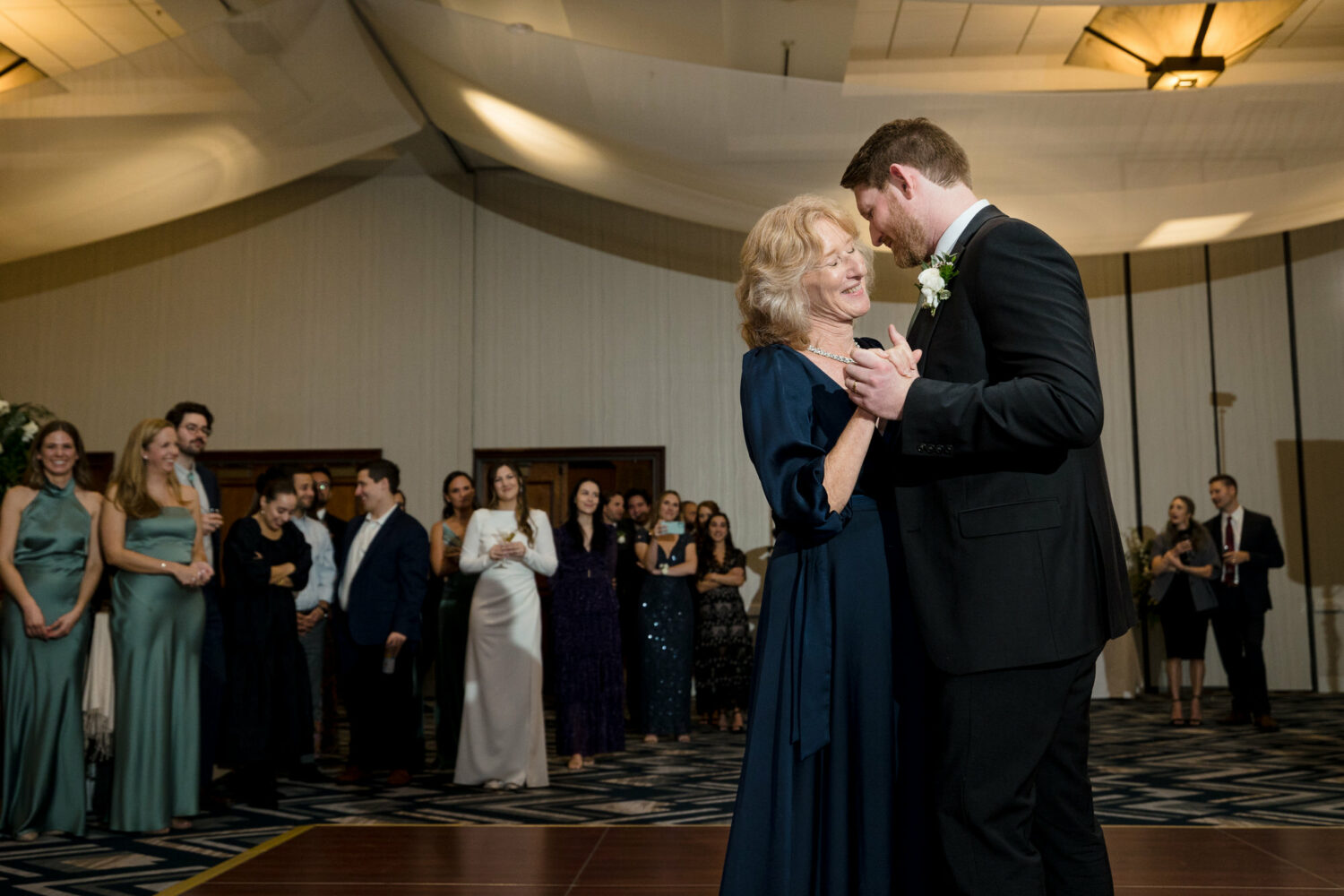 The mother of the groom dances with her son at an Everline Resort indoor reception.