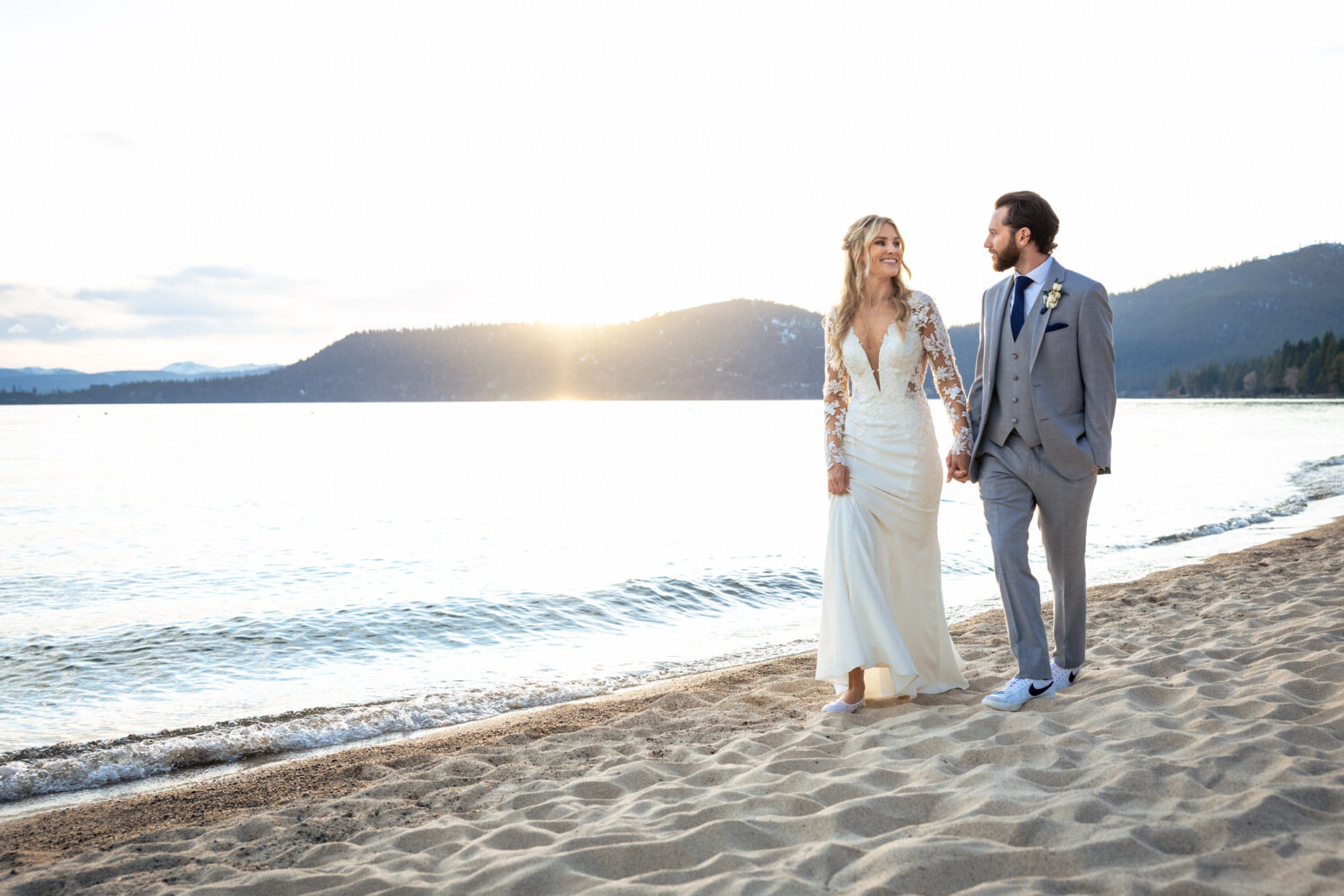 A bride and groom enjoy a sunset stroll by the water at their Hyatt Lake Tahoe beach wedding.