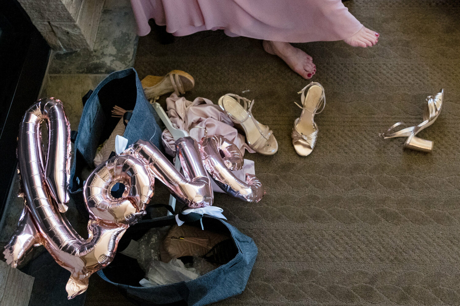 A stressful wedding day scene: tired feet, disorganized bridal party gift bags, and a balloon that spells "LOVE" laying on the floor.