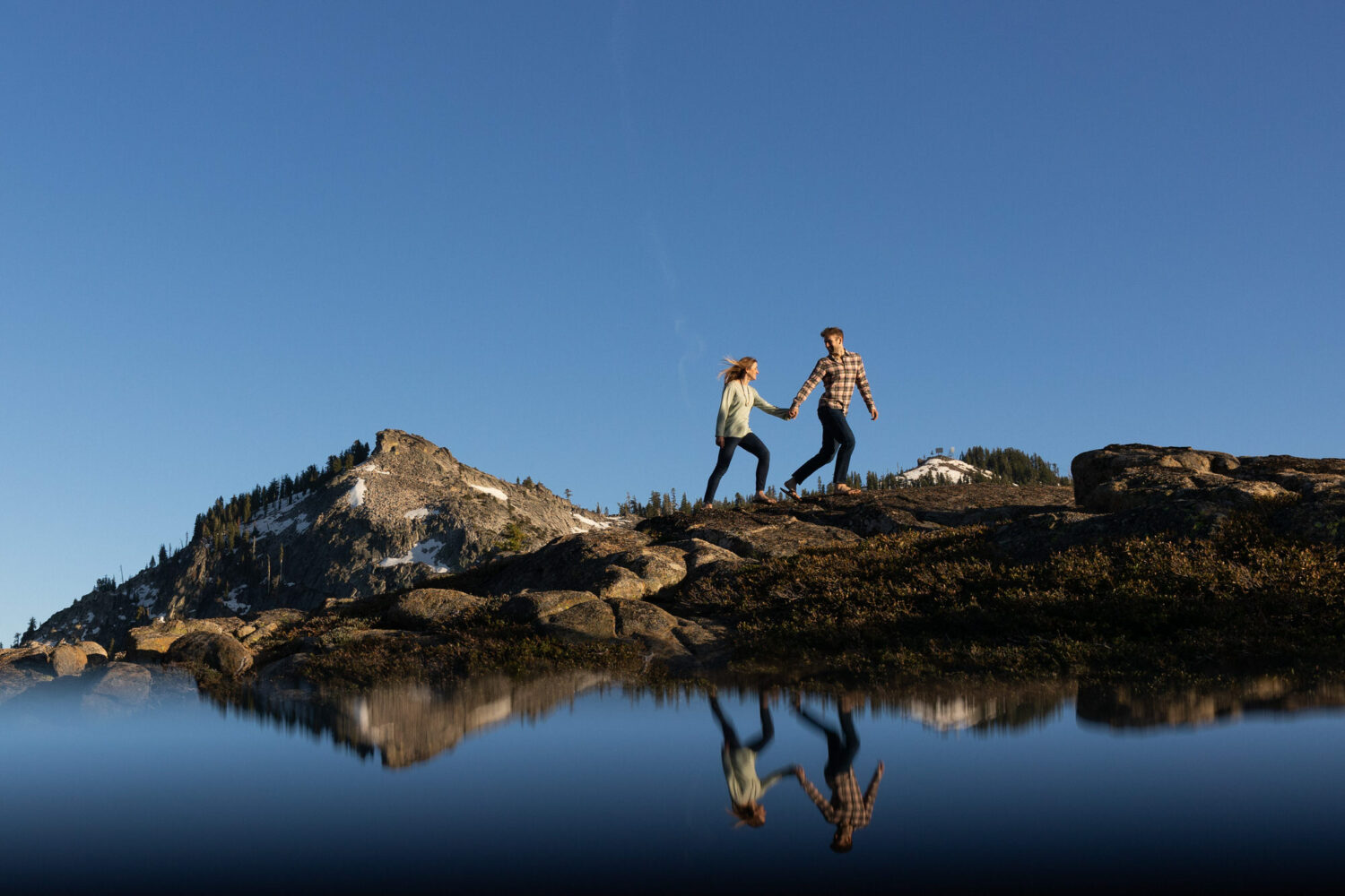 A couple walks hand in hand along a granite ridge during engagement photos near Donner Peak.