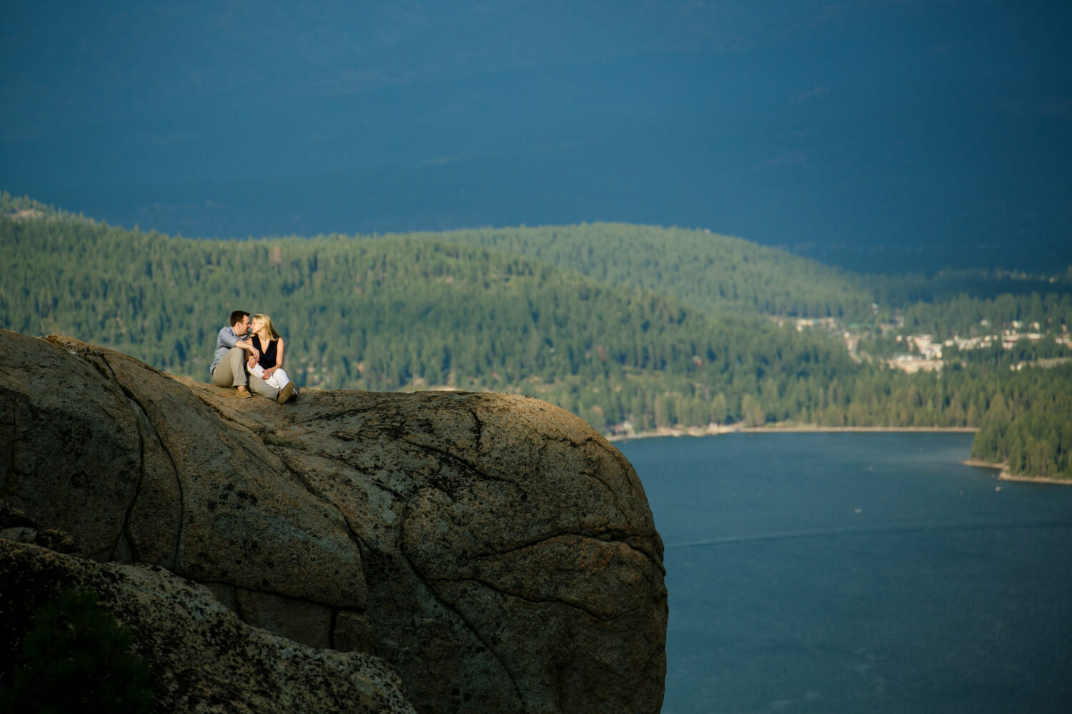 A romantic moment for a couple during an engagement photoshoot on a mountaintop with forests and a lake in the background. 